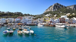 A coastal town with a marina filled with boats, white buildings, and a prominent mountain in the background. - Donna Rosa Capri - Charming House by the Sea (Capri)