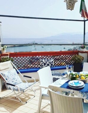 A balcony with a view of the sea, a table set with plates and a vase of flowers, and two chairs. - Donna Rosa Capri - Charming House by the Sea (Capri)