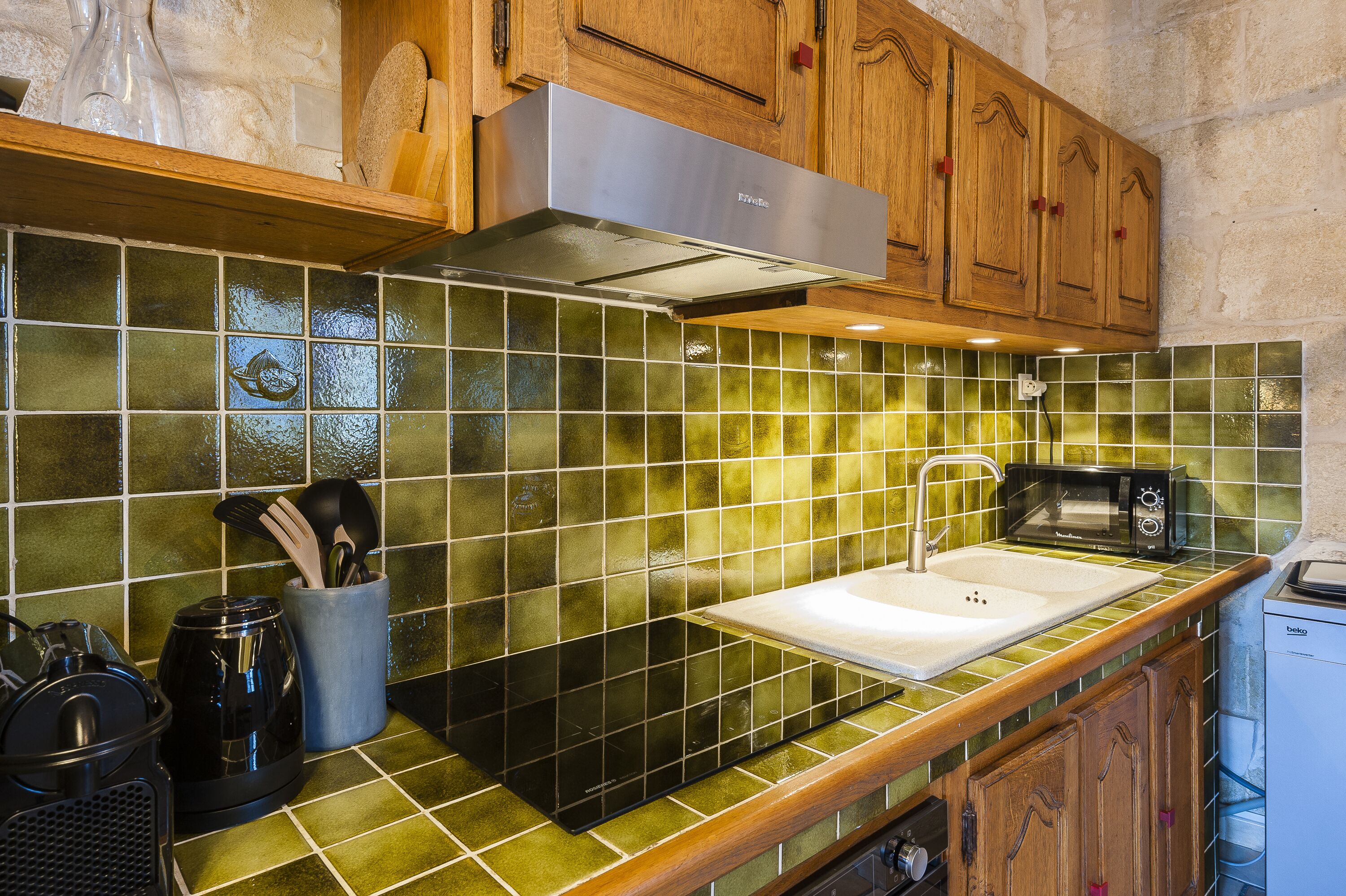 A kitchen with green-tiled backsplash, wooden cabinets, a stainless steel range hood, a microwave, and a dishwasher.