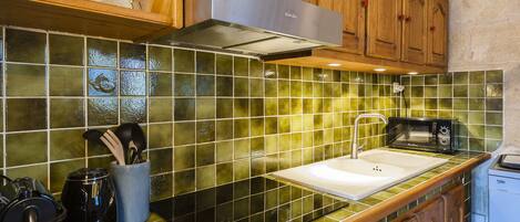 A kitchen with green-tiled backsplash, wooden cabinets, a stainless steel range hood, a microwave, and a dishwasher.