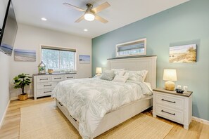Une chambre à coucher comprenant un lit, des tables de chevet, un ventilateur de plafond et des œuvres d’art accrochées aux murs.