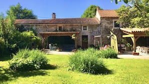 A stone house with a tiled roof, a covered patio, and a well-maintained garden. - Family friendly gîte set in idyllic countryside w/games barn + 12x6m pool (La Chapelle pouilloux)