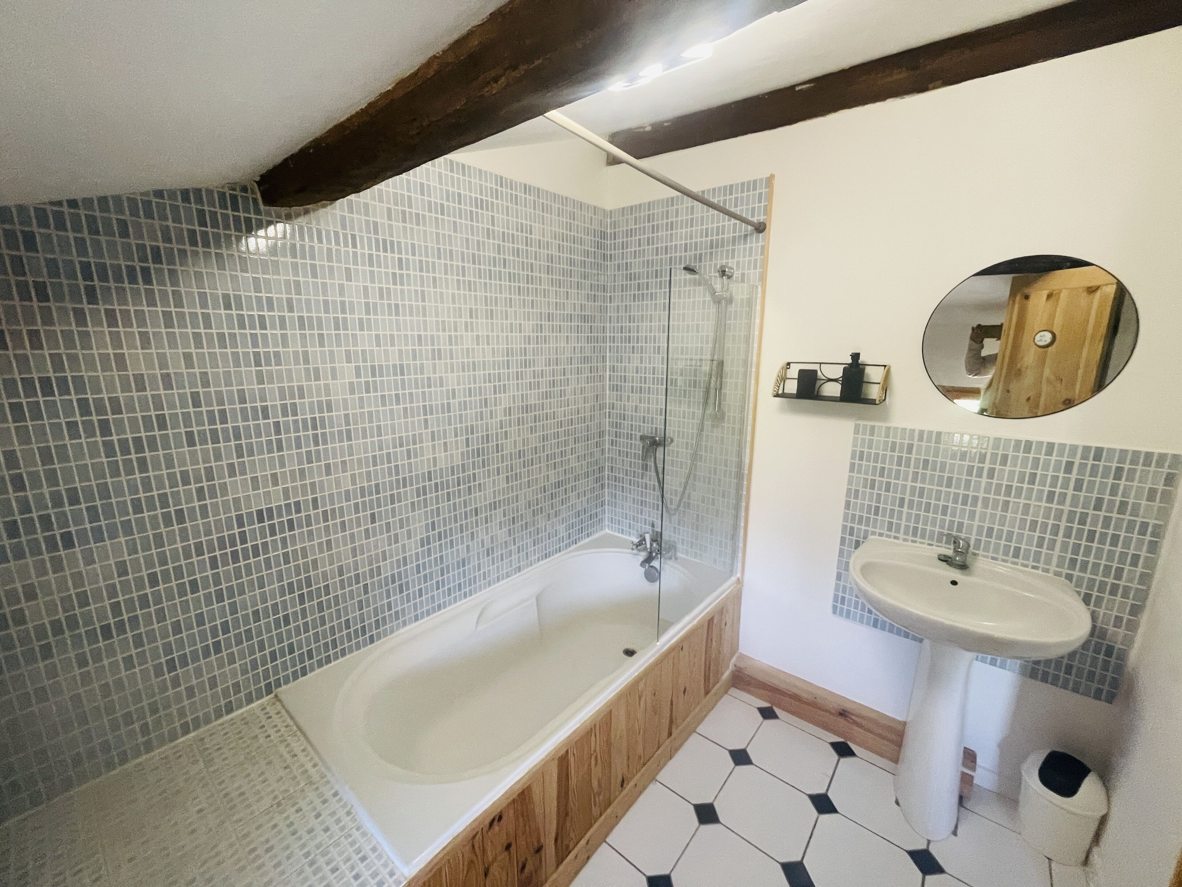 A bathroom with a glass-enclosed shower, a freestanding bathtub, a pedestal sink, and a round mirror.