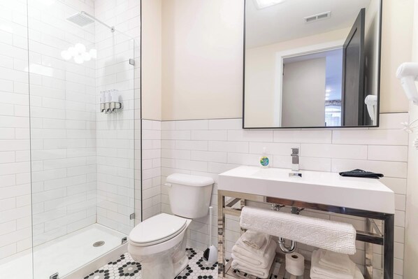 A modern bathroom with a glass shower enclosure, a white toilet, a sink with a mirror above it, and a towel rack with towels.