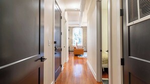 A hallway with wooden flooring, a bed with a white headboard, and a window with a view of the outdoors. - 2 Bedroom Suite (Frankfort)