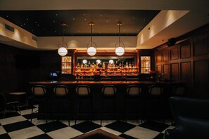 A bar area with a checkered floor, bar stools, and a well-lit bar counter with bottles. - 2 Bedroom Suite (Frankfort)