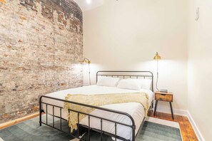 A bedroom with a brick wall, a metal bed frame, two bedside lamps, a bedside table, and a rug. - 2 Bedroom Suite (Frankfort)