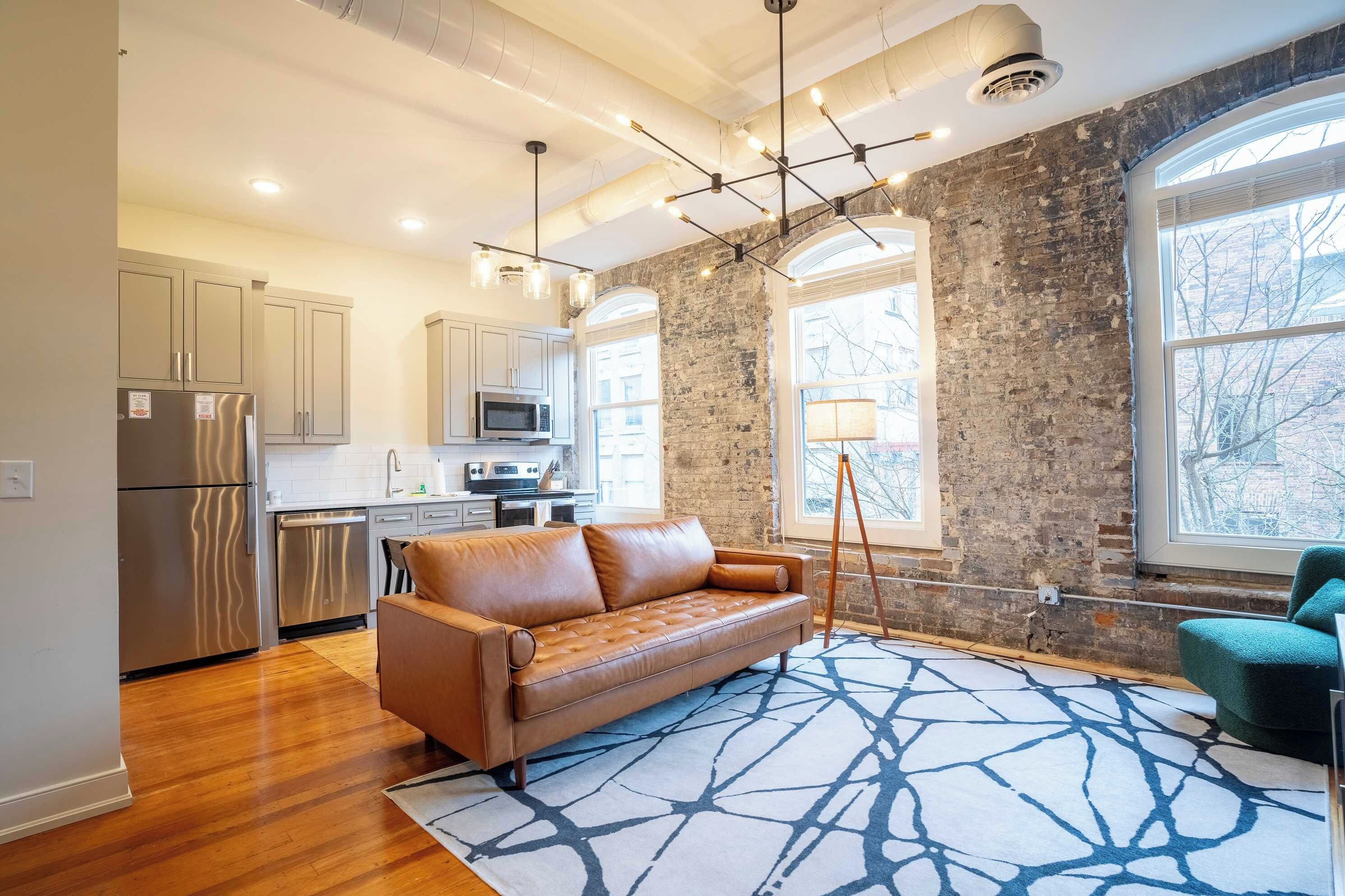 A modern kitchen with stainless steel appliances, a leather sofa, and a patterned rug.
