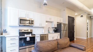 A modern kitchen with white cabinets, stainless steel appliances, and a brown sofa in the living area. - 2 Bedroom Suite (Frankfort)