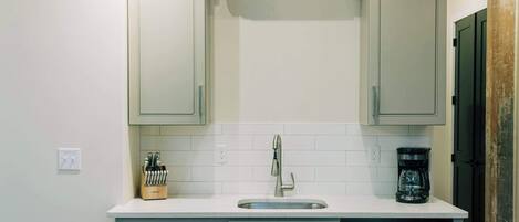 A modern kitchen with a built-in oven, microwave, and dishwasher, a white countertop, and a wooden dining table.