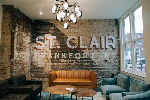 A room with a brick wall, a large sign reading 'THE ST. CLAIR ANKFORTH KY', a brown sofa, a blue sofa, and a wooden coffee table.