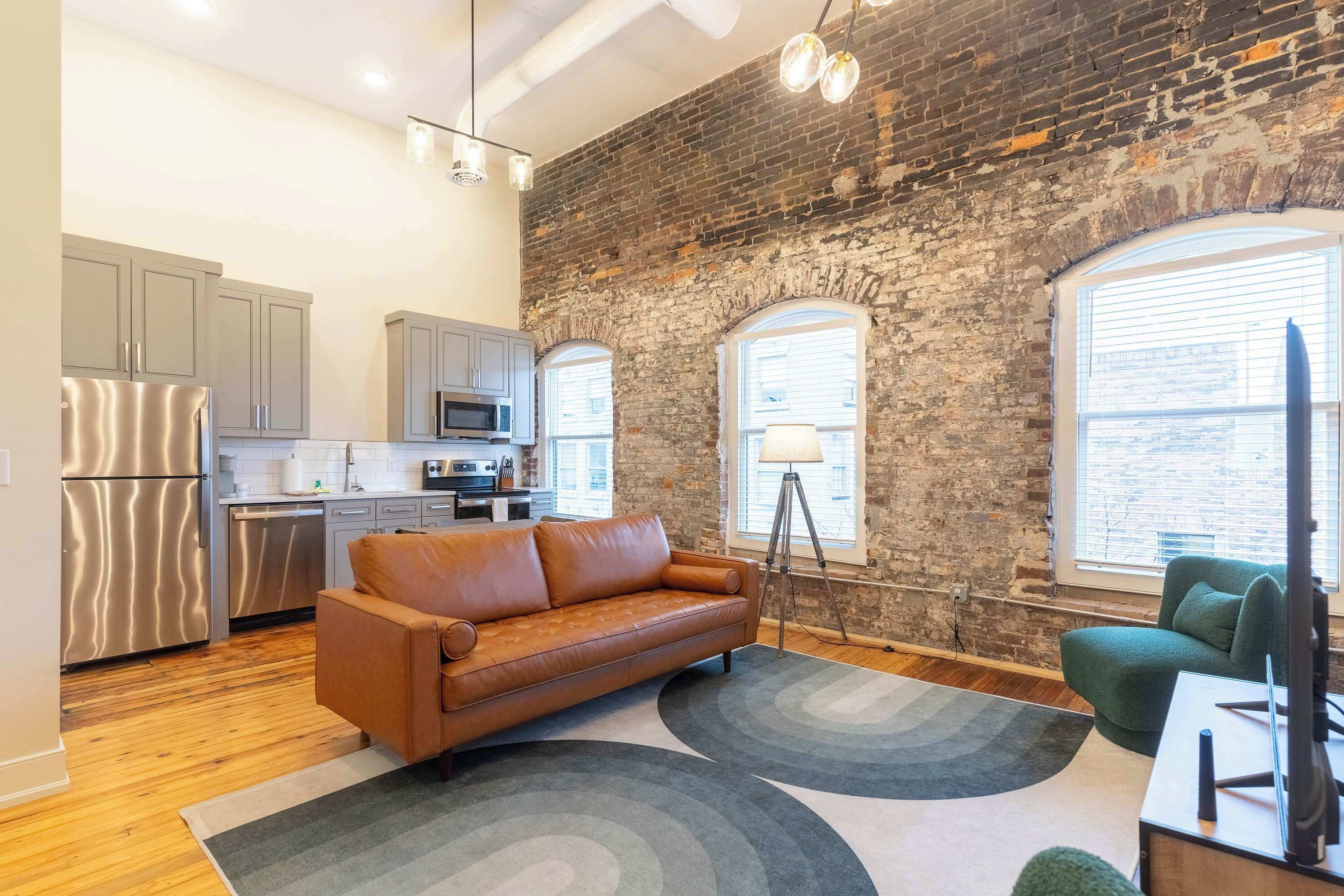 A modern kitchen with stainless steel appliances, a brown leather sofa, and a green armchair.