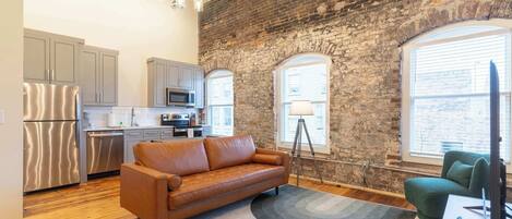 A modern kitchen with stainless steel appliances, a brown leather sofa, and a green armchair.