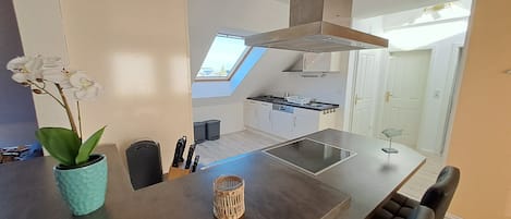 Una cocina moderna con tragaluz, una zona de comedor con mesa, sillas y un jarrón de flores blancas.