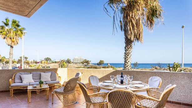 A terrace with wicker furniture, a table set for dining, and a view of the sea.