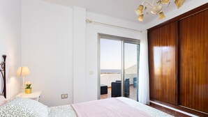 A bedroom with a bed, a nightstand, a lamp, a window, and a view of the outside.