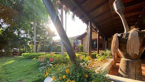 A garden with a stone planter filled with marigolds, a wooden structure with a thatched roof, and a large stone basin with hanging plants.