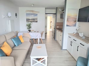 A modern living room with a sofa, coffee table, and dining area. There is a kitchen with cabinets and a TV. - Les Mouettes Marines Bénodet : Appartement vue mer (50 m de la plage) (Benodet)