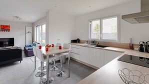A modern kitchen with white cabinets, a dining area with a table and chairs, a black countertop, and a window providing natural light. - Rosamaris - Maison pour 8 avec jardin (Saint-Malo)