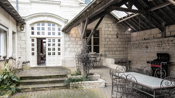 Un cortile con un edificio in pietra, una zona relax coperta e un barbecue.