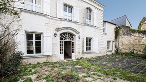 Un edificio bianco con un ingresso ad arco centrale, ampie finestre e un muro in pietra sulla destra.