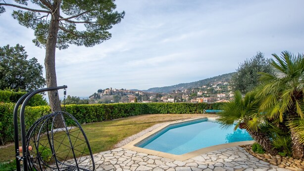 Une piscine aux bords recouverts de pierres, entourée de verdure et offrant une vue sur une ville lointaine.