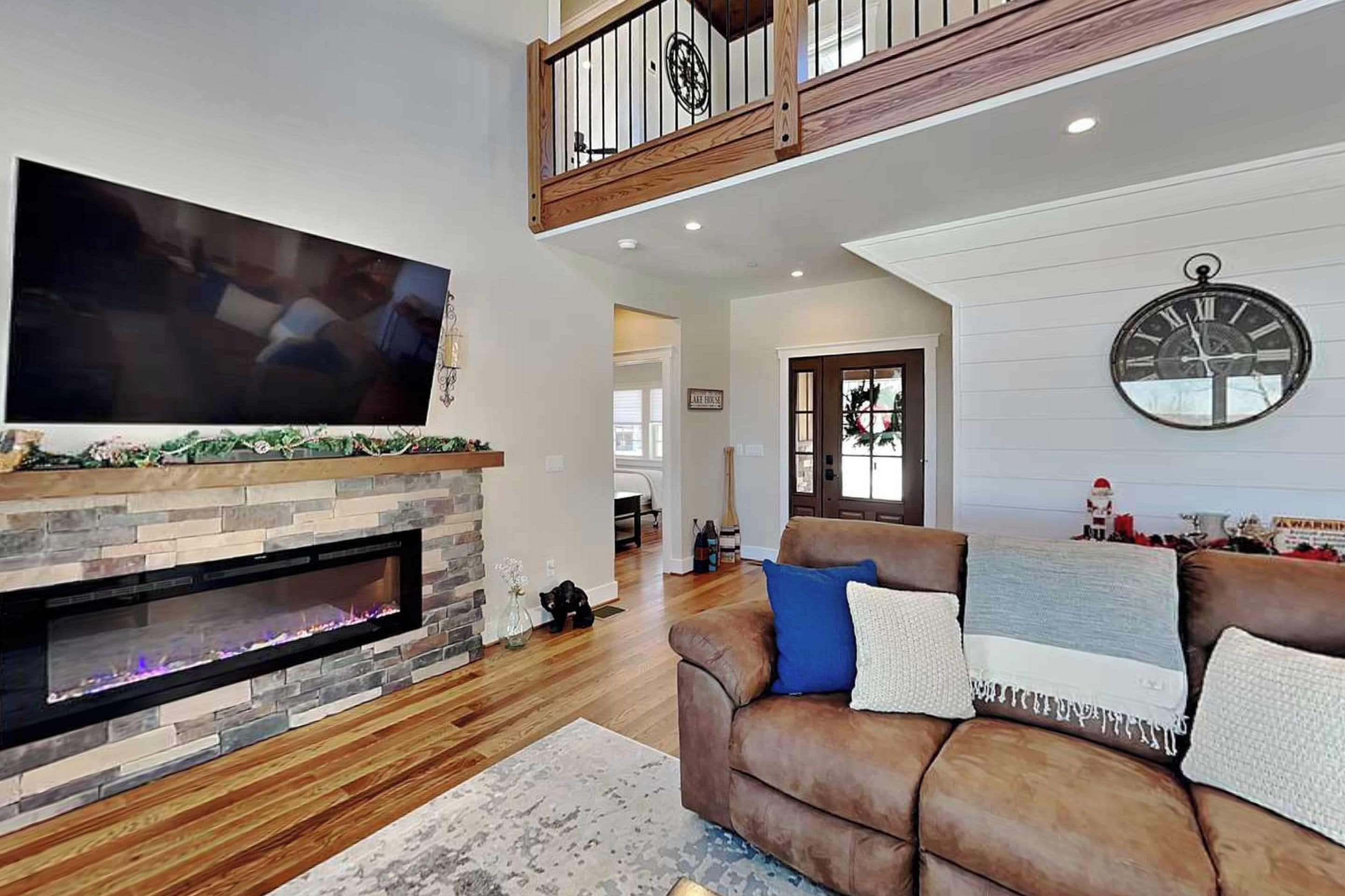 A living room with a fireplace, a large flat-screen TV, a leather sofa, and a wooden staircase.