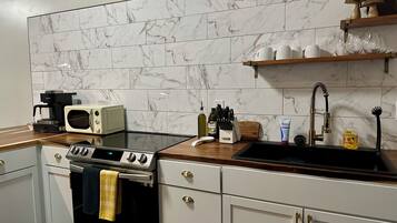 A kitchen with a black stove, white cabinets, a microwave, and a sink with a faucet.