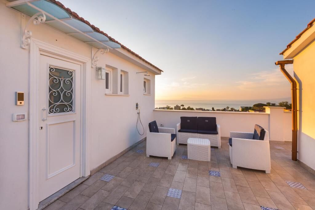 A rooftop terrace with white wicker furniture, a door with decorative glass, and a view of the sea at sunset.