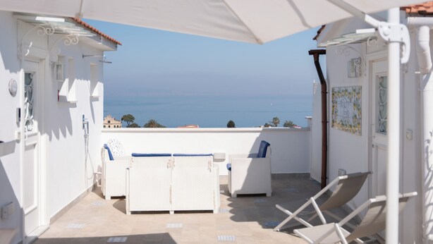 A balcony with white furniture, a white umbrella, and a view of the sea. - BEAUTY HOME SORRENTO (Sorrento)
