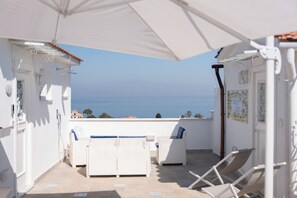 A balcony with white furniture, a white umbrella, and a view of the sea. - BEAUTY HOME SORRENTO (Sorrento)