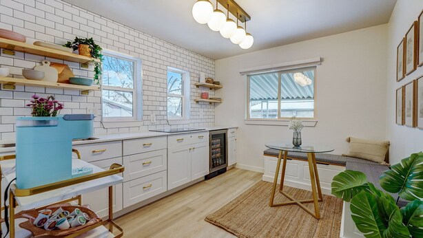 A modern kitchen with white cabinets, a built-in oven, and a coffee machine. There is a dining area with a table and chairs, and a window with a view of the outside. - The Oakley House (Salt Lake City)