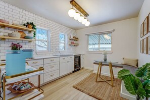Una cocina moderna con armarios blancos, horno empotrado y cafetera. Cuenta con un comedor con mesa y sillas, y una ventana con vistas al exterior.