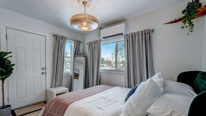 A bedroom with a bed, a bedside table, an air conditioning unit, a window with curtains, and a potted plant. - The Oakley House (Salt Lake City)