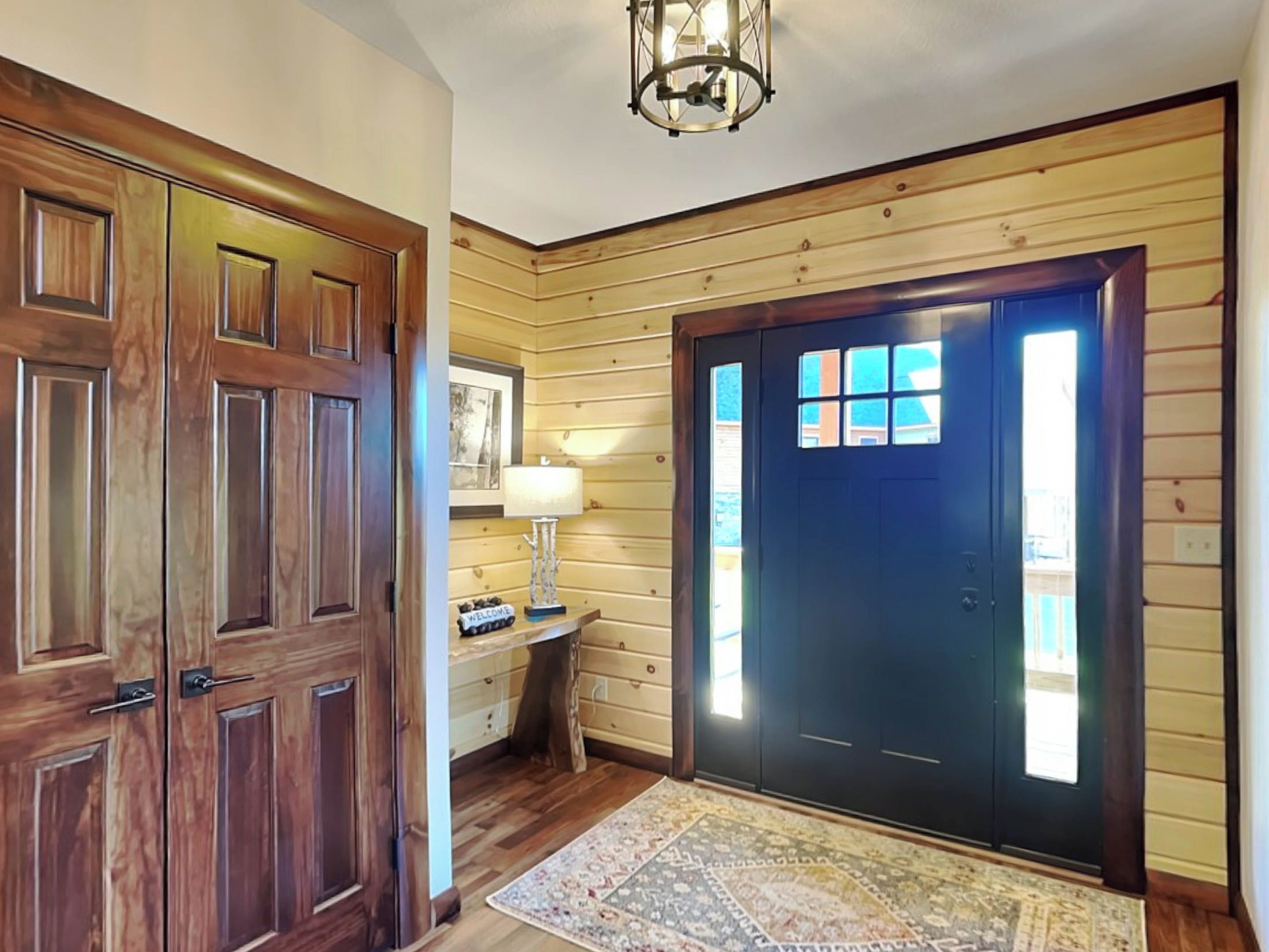 Un interior de madera con una puerta azul oscuro, un letrero de bienvenida y una lámpara.