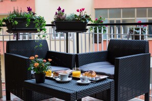 A balcony with wicker furniture, a breakfast setup including croissants, coffee, and orange juice, and potted plants. - Rome By Suite Vatican (Rome)