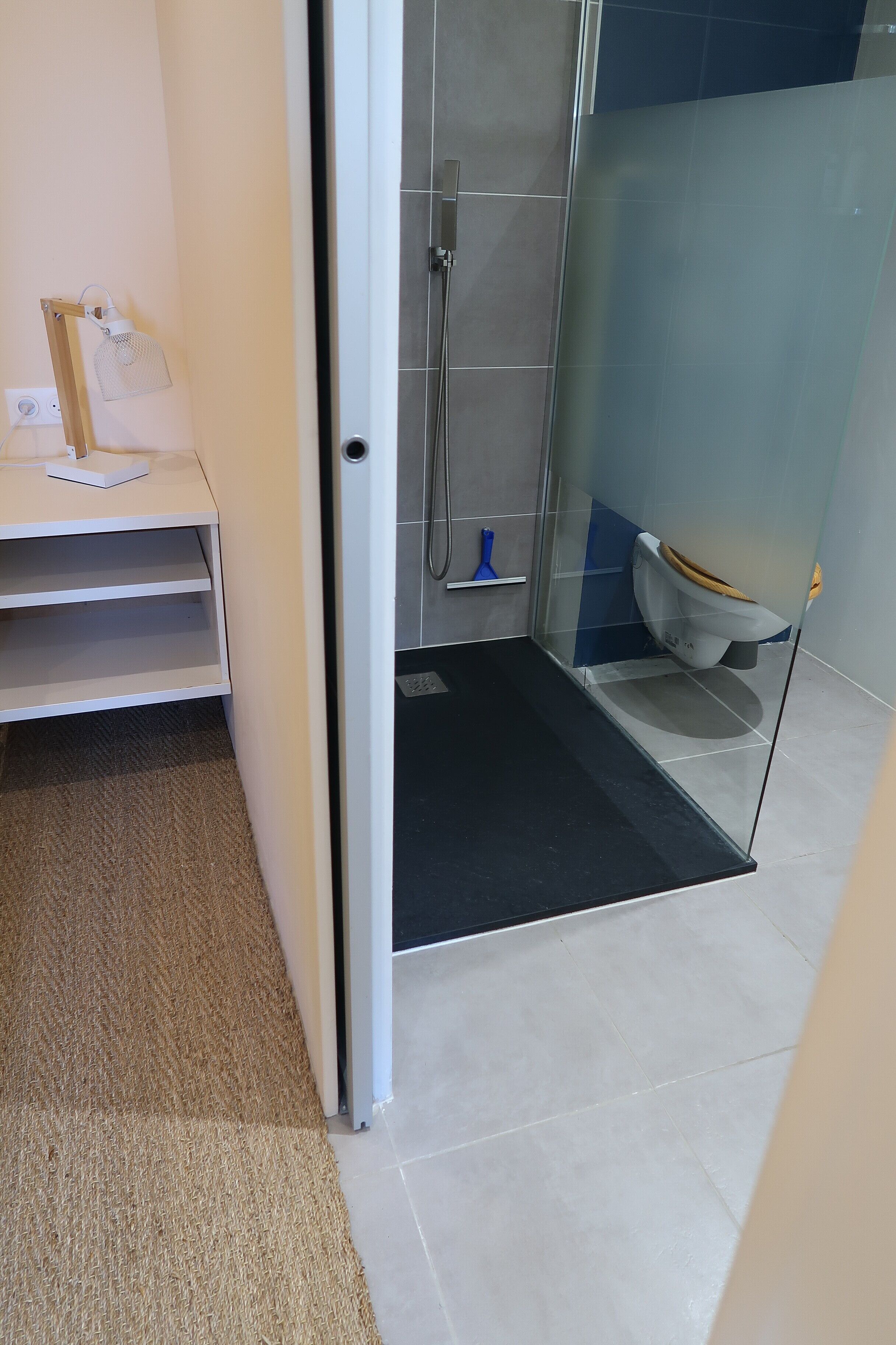 Un bagno moderno con box doccia in vetro, un water e un piccolo ripiano con una borsa e un quaderno.