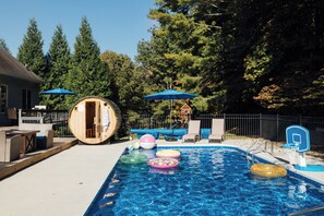 Une piscine avec des bouées gonflables, une structure en bois et des chaises longues.