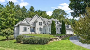 A large, two-story house with a well-maintained lawn, a stone retaining wall, and a driveway leading to the garage. - 8BR Resort Estate with Pool and Theater (Fletcher)