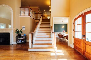 Un hall d’entrée spacieux avec un escalier en bois, une cheminée et un coin repas offrant une vue sur la cuisine.