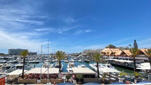 A marina with numerous boats docked, a large building with a pyramid-like structure, and outdoor seating areas with umbrellas.