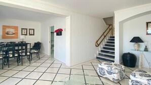 A spacious living area with a dining table and chairs, a staircase, and a glass coffee table.
