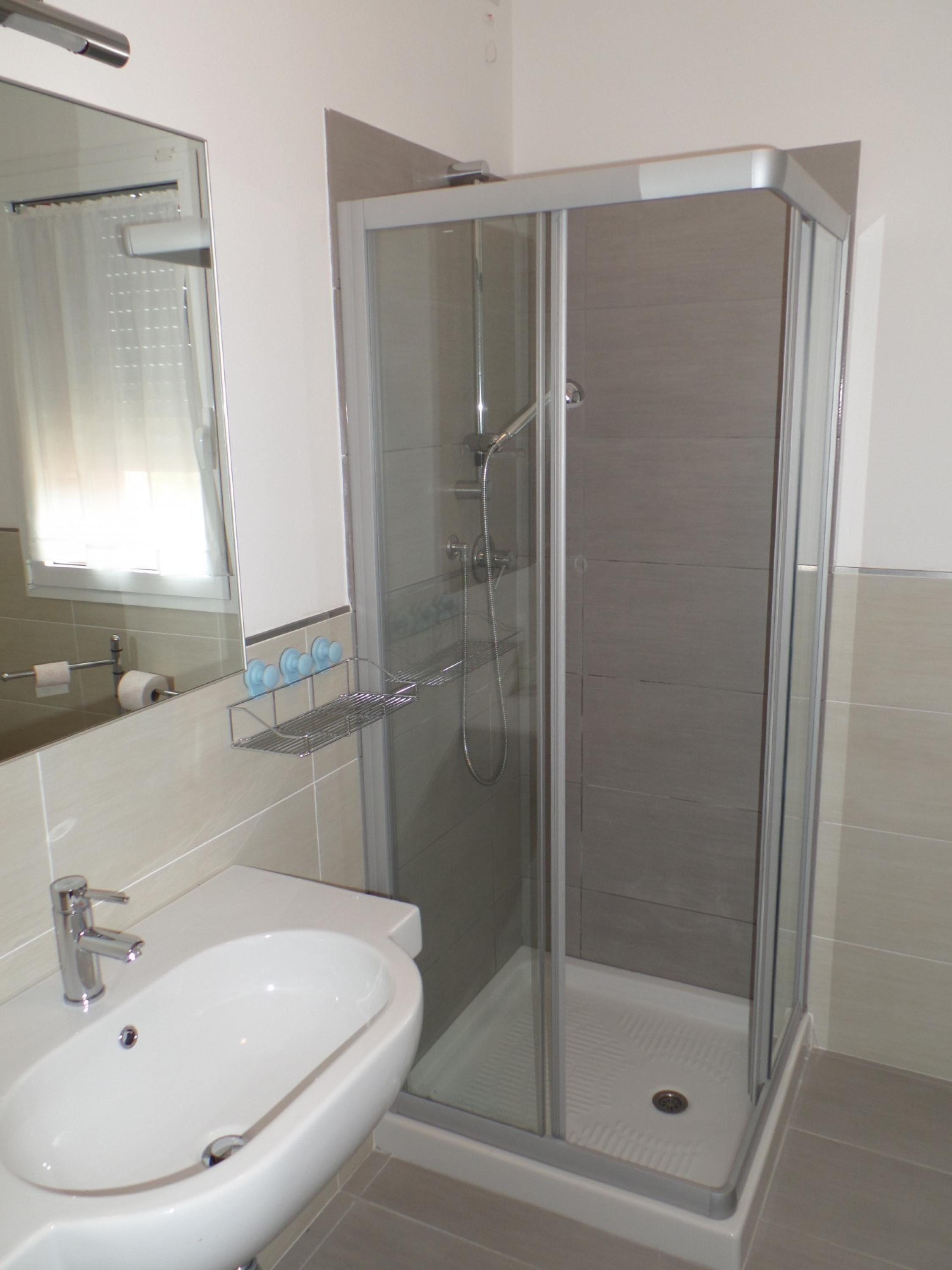 Casa de banho moderna com cabine de duche em vidro, lavatório branco e espelho sobre o lavatório.