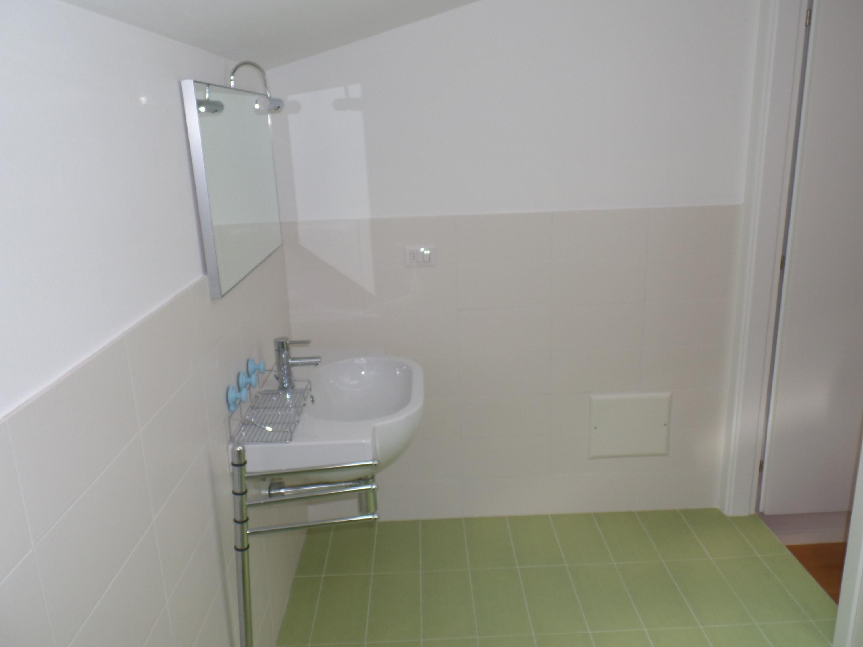 A bathroom with a sink, mirror, and green-tiled floor.