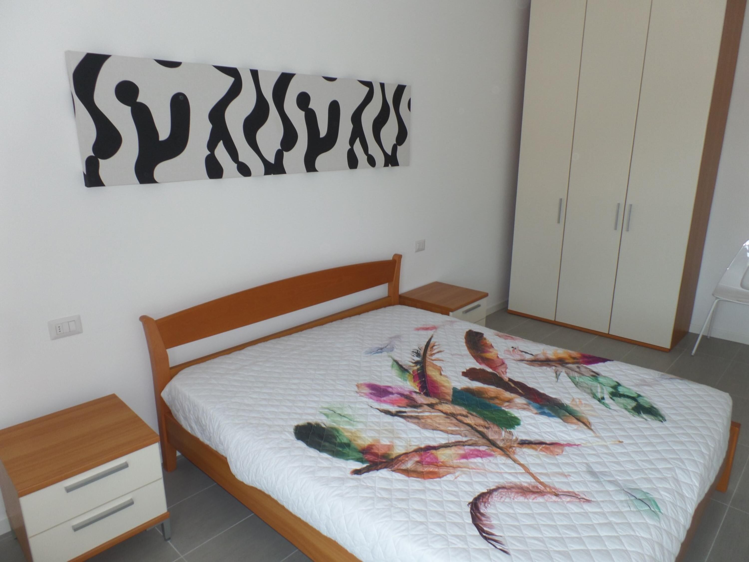 A bedroom with a wooden bed, a nightstand, a wardrobe, and a wall art piece.
