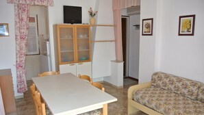 A dining area with a table and chairs, a sofa, a cabinet with glass doors, and a television on a stand.