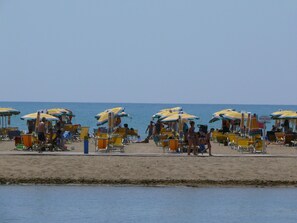 A beach with rows of sun umbrellas and beach chairs. - Condominio Giardino C (San Michele al Tagliamento)