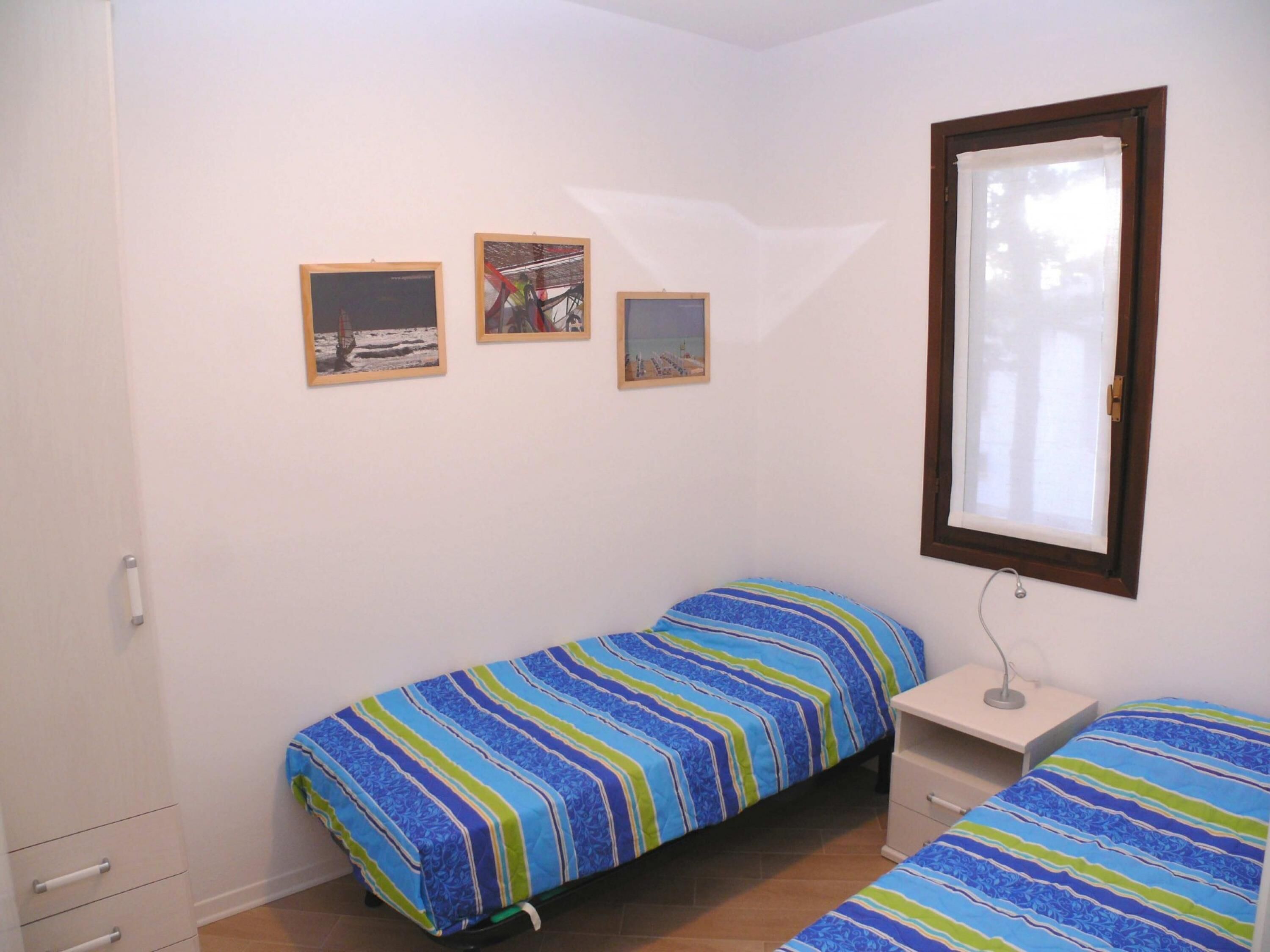 A small, single-room accommodation with a bed, a nightstand, and three framed pictures on the wall.