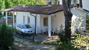 Un bâtiment blanc avec un toit recouvert de tuiles, une voiture garée et des sièges à l’extérieur.
