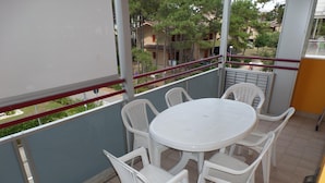 A balcony with a round table and four chairs, a red railing, and a view of buildings and trees. - Felice C in Bibione With 2 Bedrooms and 2 Bathrooms (San Michele al Tagliamento)
